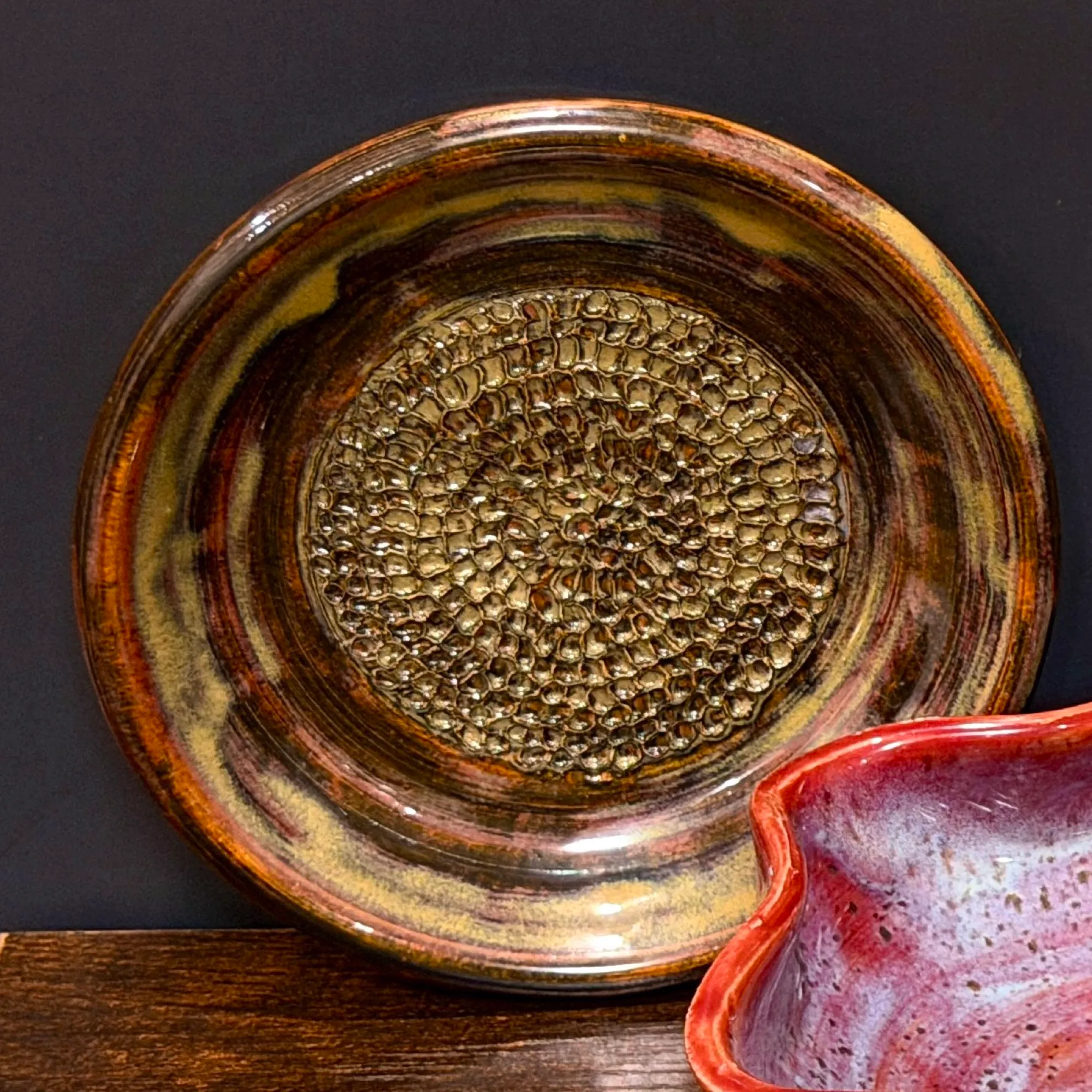 A round amber and brown plate with a field of small raised teeth in its center for grating garlic.