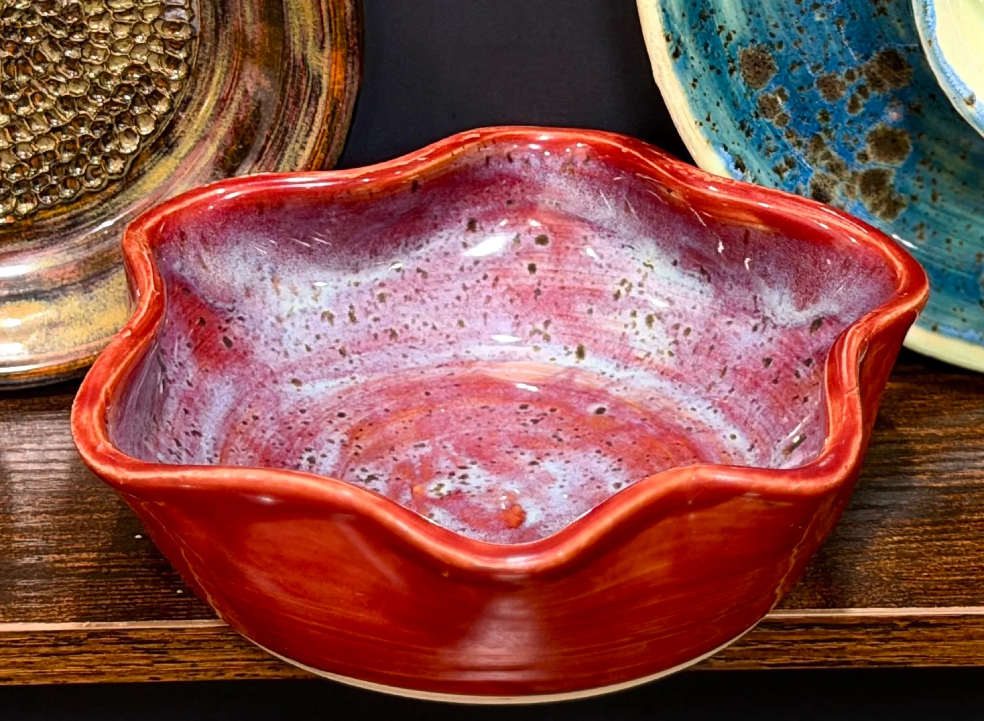 A red bowl with a wavy, star-shaped rim and a speckled pink and lilac glaze inside.