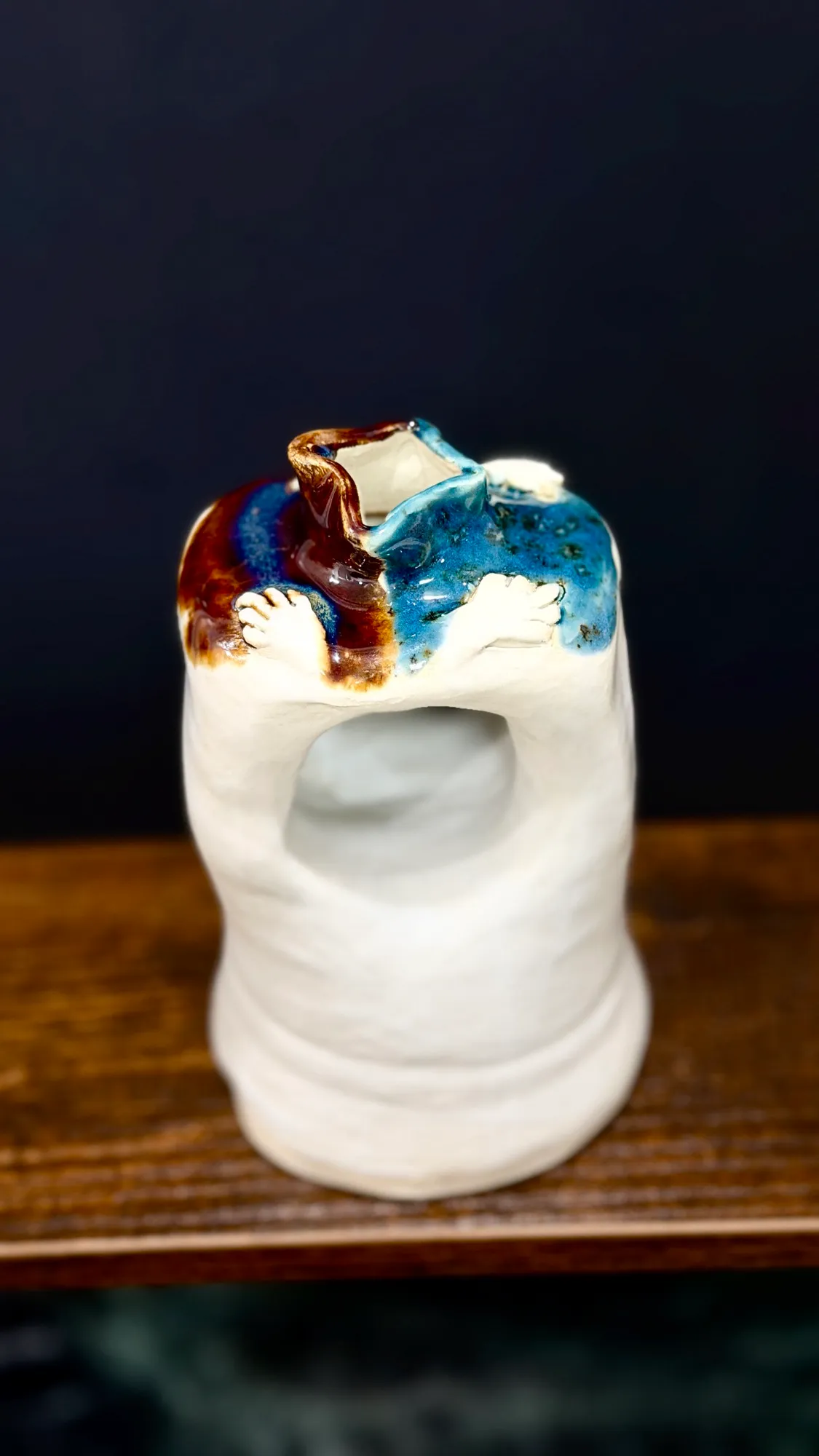 Close-up of The Hug, a white vessel with two small sculpted hands reaching around its glazed top and an open hollow through its middle.